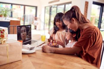 Asian Family Celebrating Birthday At Home With Father Working Away Via Video Call