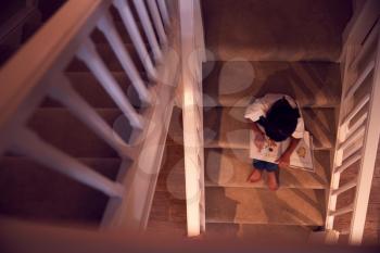 Overhead View Of Asian Girl Sitting On Stairs At Home Reading Book