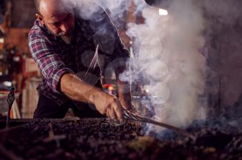 Male Blacksmith Raking Coals Fuel To Start Blaze In Forge