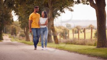 Front View Of Loving Couple Hugging As They Walk Along Track Through Countryside