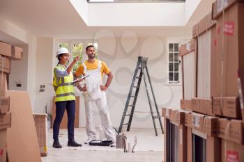 Female Surveyor With Clipboard Meeting With Decorator Working Inside Property