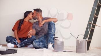 Loving Couple Taking A Break As They Decorate Room In New Home Together