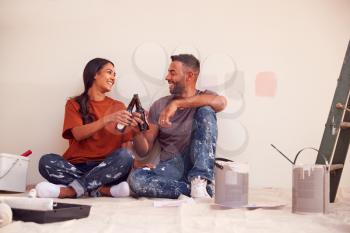 Couple Taking A Break And Drinking Beer As They Decorate Room In New Home Together