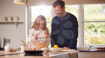 Father And Daughter Wearing Pyjamas Making Pancakes In Kitchen At Home Together