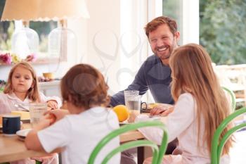 Father With Children Wearing Pyjamas Sitting Around Table Enjoying Pancake Breakfast Together