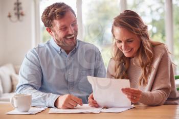 Smiling Couple Sitting At Table At Home Reviewing Domestic Finances