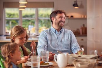 Father And Children Sitting Around Table At Home Enjoying Meal Together