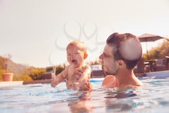 Father With Baby Daughter Having Fun On Summer Vacation Splashing In Outdoor Swimming Pool