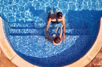 Overhead Shot Of Father With Young Son Having Fun On Summer Vacation In Outdoor Swimming Pool