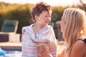 Mother Wrapping Son In Towel By Outdoor Swimming Pool On Summer Vacation