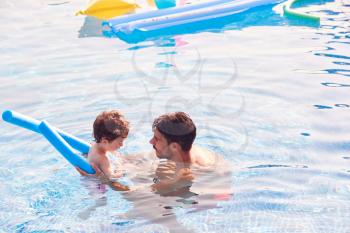 Father And Son In Outdoor Pool On Summer Vacation Teaching Son To Swim With Noodle Swimming Aid