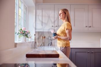 Mature Woman At Home With Hot Drink Standing By Kitchen Window