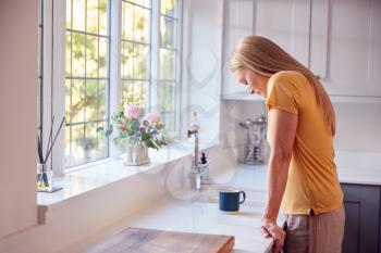 Depressed And Unhappy Mature Woman At Home Standing By Kitchen Window