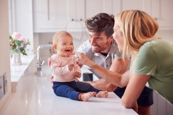 Family With Baby Daughter Having Fun Playing Game Sitting In Kitchen Together