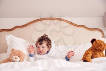 Young Boy Lying In Parents Bed With Cuddly Teddy Bear Toys