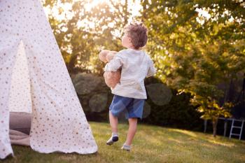 Young Boy Carrying Teddy Bear Having Fun With Tent Or Tepee Pitched In Garden