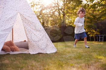 Young Boy Running And Having Fun With Tent Or Tepee Pitched In Garden