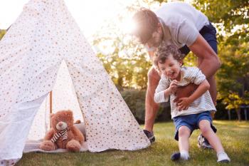 Father And Son Having Fun With Tent Or Tepee Pitched In Garden
