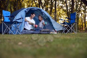 Couple In Tent Camping Sitting By Barbecue Grill And Drinking Champagne