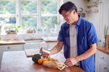 Mature Asian Man Unpacking Shopping In Kitchen At Home