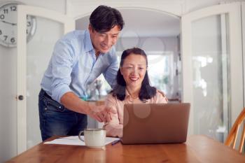 Mature Asian Couple At Home Using Laptop To Organise Household Bills And Finances