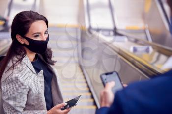 Businessman And Businesswoman Riding Escalator At Railway Station Wearing PPE Face Mask In Pandemic