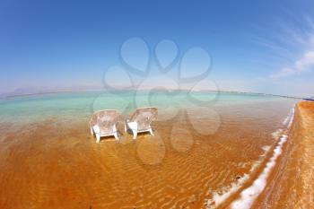 Two white beach chairs stood side by side in the clear water at the beach. Dead Sea, Israel