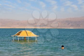 The brave bather plunged into the cool water from the Dead Sea. Sunny beach on the Dead Sea. A wonderful warm day in December. The beach pavilion is half flooded with seawater risen