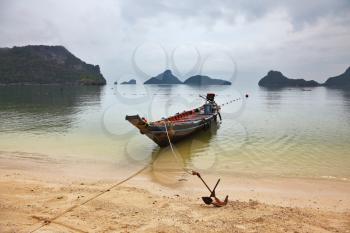 Thai Longtail boat moored on a sandy beach with an anchor. Picturesque bay on the island surrounded by islands
