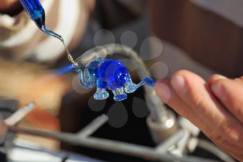Delicate work of the glass blower. The Artist-glass blower produces a graceful tiny figure of an elephant from color glass