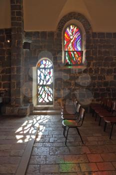 The interior of an ancient church on the shore of the Sea of ​​Galilee. A magnificent stained glass window and glass door illuminated by the sun.