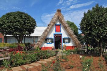 Pastoral landscape. Cosy chalet with a triangular thatched roof. Before the house - garden with beautiful flower beds. Madeira, the city of Santana