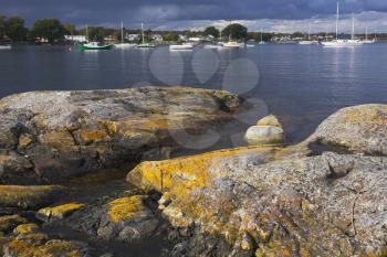 Picturesque coastal stones on coast of ocean passage, overgrown mosses, and sailing yachts