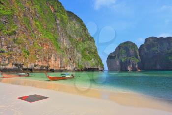 Picturesque green islands of the Thai coast. Emerald sea and thin white sand. In sand two tourist boats, decorated with multi-colored silk scarfs and wreaths are moored