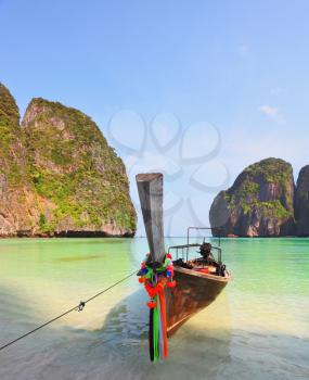 Scenic green islands of Thailand coast. Emerald sea and fine white sand. Moored on the beach tourist boat, decorated with red silk scarf and a flower wreath