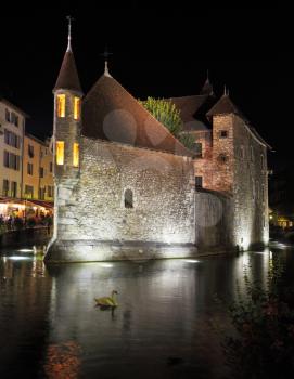 Old fortress-prison on the island in the middle of the river. Castle illuminated by spotlights and is beautifully reflected in the dark water. In the river white swans float. Summer night in the charm