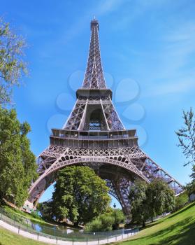 The most famous in the world - the Eiffel Tower in the background of bright blue sky. At the foot of the tower - a park and a large pond. The picture was taken by lens Fisheye