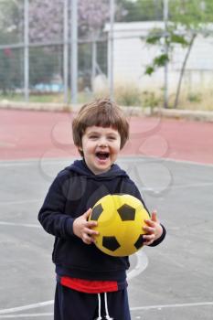 A lovely little boy played happily with a yellow ball on the playground
