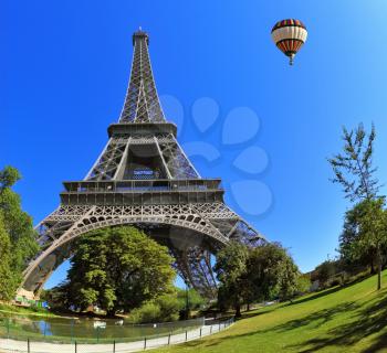 The majestic symbol of Paris - Eiffel Tower. At the foot of the tower is designed park with paths and pond. In the sky next to the tower floats giant balloon. The picture was taken Fisheye lens
