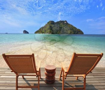 Romantic corner on the beach. Two folding wooden chairs and a small side table. Through the emerald sea water visible fine yellow sand
