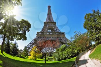 The majestic symbol of Paris - the Eiffel Tower lit hot summer sun. At the foot of the tower is designed park with paths and pond. The picture was taken Fisheye lens