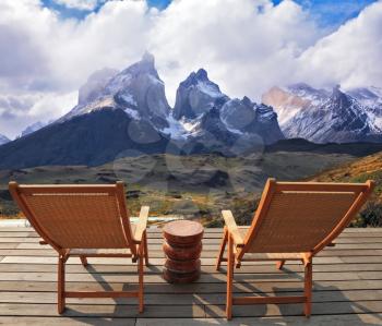 Comfortable lounge chairs on wooden platform for rest and observation. Gorgeous snow-covered rocks in the national park Torres del Paine