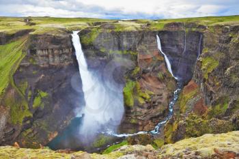 Vertical cliff, from which the powerful waterfall flies on black stones. Spectacular waterfall Hayfoss in Iceland