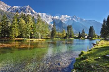 Snowy Alps picturesquely surrounded by evergreen trees and lake. Cozy urban park in Chamonix, Provence