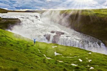  On a mountain slope the woman delighted looks at a boiling chasm. Powerful Gullfoss in Iceland. 
