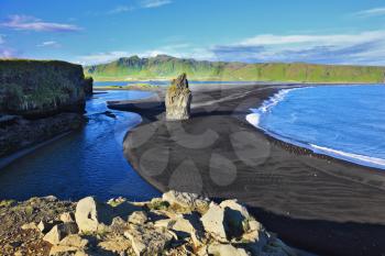 The cape Dirkholaey in the south of Iceland. On beach with black volcanic sand there is a huge rock in the form of a palm
