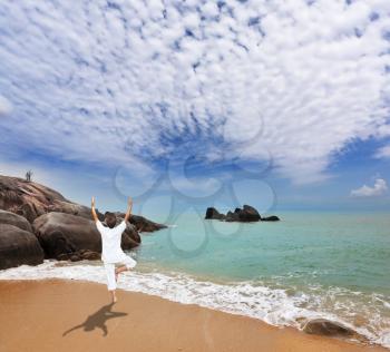 Thailand. Gorgeous beach on the Andaman Sea. Middle-aged woman dressed in white doing yoga. 
Pose Tree, stand on one leg