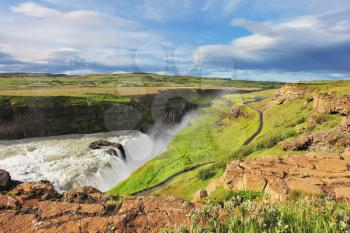 Grand Gullfoss in Iceland. Summer sunny day. Roaring water lit by the morning sun. The river banks are overgrown with green moss northern