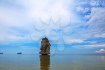 Island Sail in the ocean. The blue haze of the warm sea - background for the huge stone cliff. The island is reflected in the smooth surface of the water
