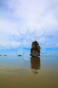 The haze of warm sea - background for huge stone cliff. Island Sail in the ocean. The island is reflected in smooth surface of water